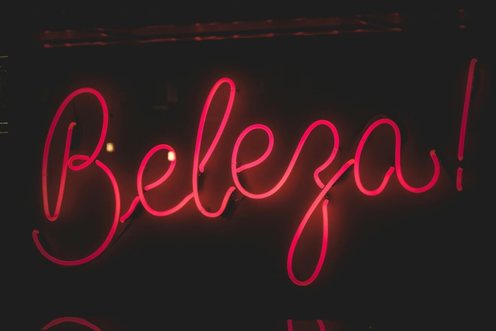 Vibrant pink neon sign with 'Beleza!' text on a black background, creating a striking visual appeal.